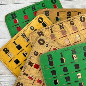 May include: Five vintage wooden bingo cards with green and yellow backgrounds. The cards have the letters B, I, N, G, and O printed on them. Each card has a grid of squares with numbers printed in red and black. The cards are stacked on top of each other. The bottom card has a sticker with the text "Veterans of Foreign Wars Post No. 301 Tennessee".