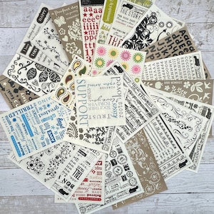 May include: A collection of vintage-style scrapbook paper sheets with various designs and patterns. The papers feature black and white illustrations, including flowers, hearts, and words like "support", "trust", and "love". Some sheets have a brown background with white text and illustrations.