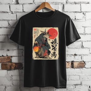 May include: Black t-shirt featuring a wolf-like figure in traditional Japanese attire, holding a lantern. The design includes a red sun and Japanese text. The shirt is hanging on a wooden hanger.