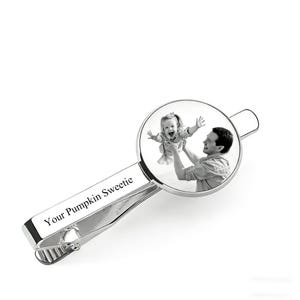 May include: A silver-colored tie clip with a circular photo of a person holding a child. The text "Your Pumpkin Sweetie" is engraved on the clip. The clip is designed to fasten to a shirt.