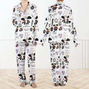 May include: White pajama set with a repeating pattern of black umbrellas, musical instruments, hearts, and text that reads "in all of us" and "Practical Magic". The long-sleeved top and pants are made of a soft material.