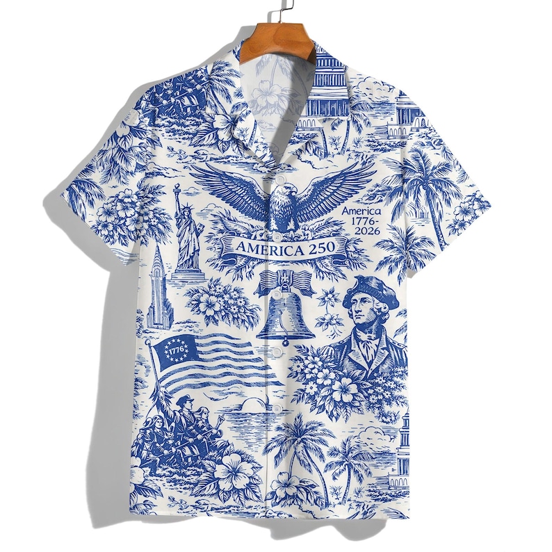 May include: White and blue button-down shirt with a patriotic design. The shirt features illustrations of the American flag, the Statue of Liberty, an eagle, and other patriotic symbols. The text "America 250" is also visible.