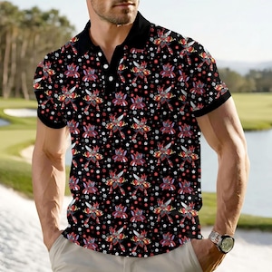 Può includere: Polo nero con un motivo ripetuto di figure simili a robot rosse e viola e accenti bianchi a forma di stella. La camicia ha un colletto nero e maniche corte.