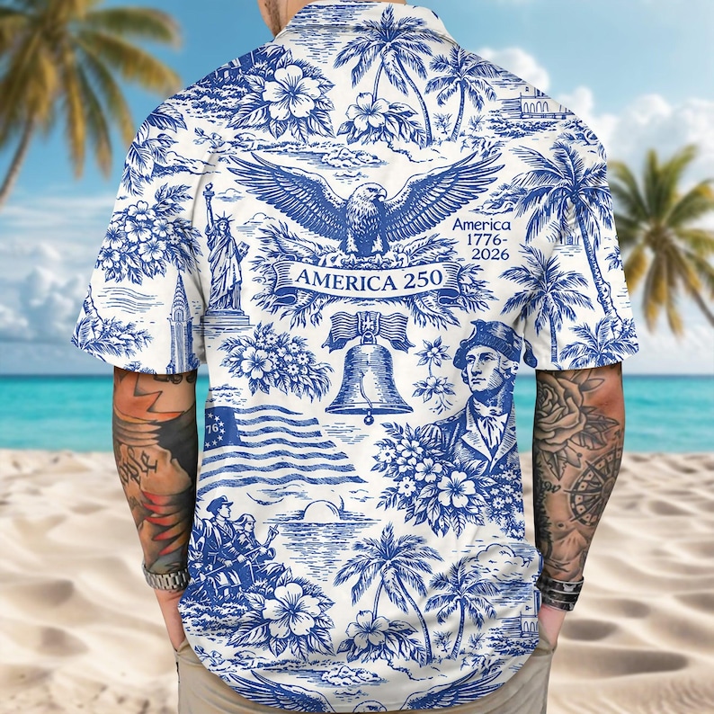 May include: White and blue button-down shirt with a patriotic design. The shirt features illustrations of the American flag, the Statue of Liberty, an eagle, and the Liberty Bell. The text "America 250" is also visible on the shirt.