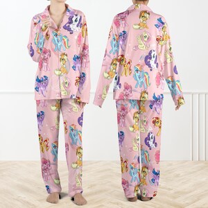 May include: A pink pajama set with a repeating pattern of cartoon ponies in various colours. The set includes a collared, button-down top with long sleeves and matching trousers. The pajamas are made from a soft, lightweight material.