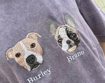 May include: A purple t-shirt features embroidered dog portraits. One dog is tan and white, the other is black and white. The names "Burley" and "Bruno" are embroidered below the dog portraits.