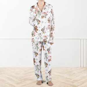 Puede incluir: Conjunto de pijama blanco con estampado de personajes de dibujos animados coloridos. La parte superior de manga larga tiene una parte delantera abotonada y un cuello con muescas. Los pantalones a juego tienen cintura el&aacute;stica. El estampado incluye varios personajes de dibujos animados y estrellas.