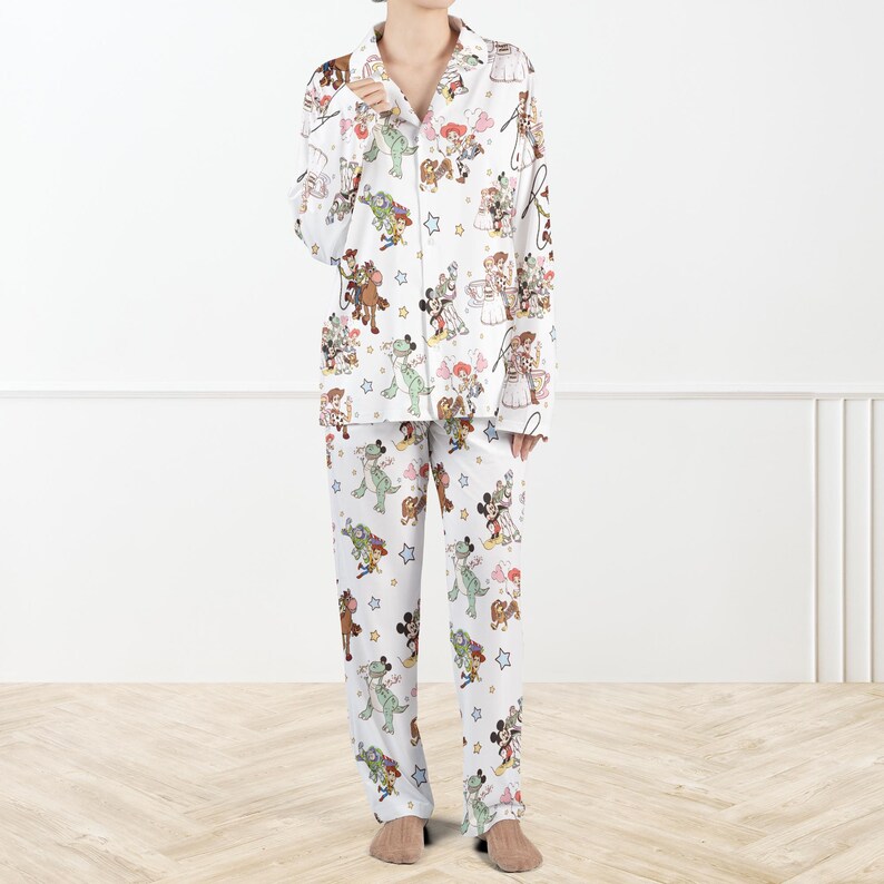 Puede incluir: Conjunto de pijama blanco con estampado de personajes de dibujos animados coloridos. La parte superior de manga larga tiene una parte delantera abotonada y un cuello con muescas. Los pantalones a juego tienen cintura el&aacute;stica. El estampado incluye varios personajes de dibujos animados y estrellas.