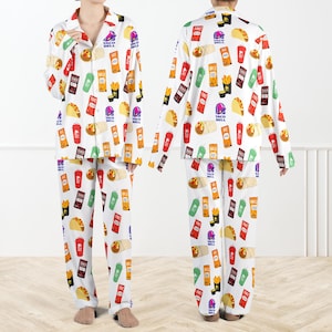May include: White pyjama set with a repeating pattern of Taco Bell food items and logos. The long-sleeved top and trousers are covered in colourful illustrations of tacos, fries, and drinks. The pyjamas have a button-down shirt style.