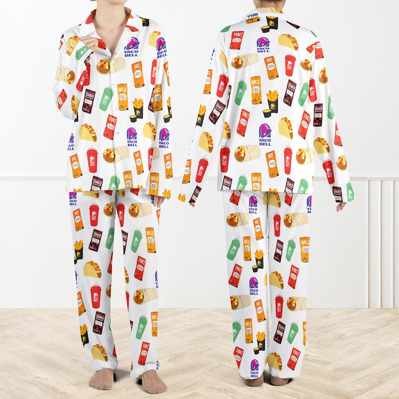 May include: White pyjama set with a repeating pattern of Taco Bell food items and logos. The long-sleeved top and trousers are covered in colourful illustrations of tacos, fries, and drinks. The pyjamas have a button-down shirt style.