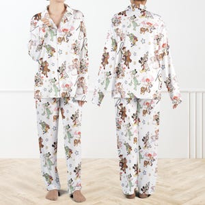 Puede incluir: Conjunto de pijama blanco con estampado de personajes de dibujos animados coloridos. La parte superior de manga larga tiene una parte delantera abotonada y un cuello con muescas. Los pantalones a juego tienen cintura el&aacute;stica. El estampado incluye varios personajes de dibujos animados y estrellas.