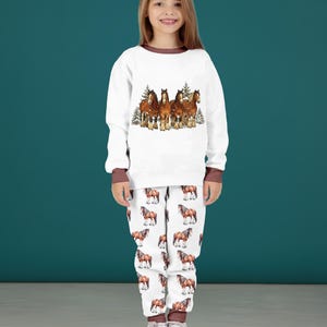 Peut inclure: Ensemble de pyjama blanc avec une bordure marron. Le haut pr&eacute;sente une image &agrave; l'aquarelle de cinq chevaux bruns avec des arbres &agrave; feuilles persistantes. Le pantalon de pyjama a un motif r&eacute;p&eacute;t&eacute; de chevaux bruns sur fond blanc. L'ensemble est en mati&egrave;re douce.