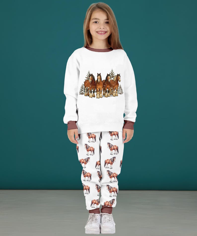 Peut inclure: Ensemble de pyjama blanc avec une bordure marron. Le haut pr&eacute;sente une image &agrave; l'aquarelle de cinq chevaux bruns avec des arbres &agrave; feuilles persistantes. Le pantalon de pyjama a un motif r&eacute;p&eacute;t&eacute; de chevaux bruns sur fond blanc. L'ensemble est en mati&egrave;re douce.