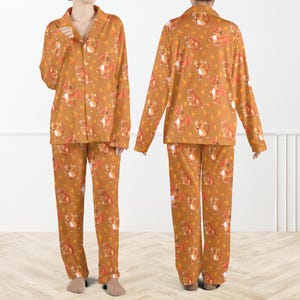 May include: A two-piece pajama set in a warm orange hue, featuring a repeating pattern of cartoon dragons in shades of red, orange, and white. The long-sleeved top has a button-down front and a collared neckline. The matching pants have a relaxed fit.
