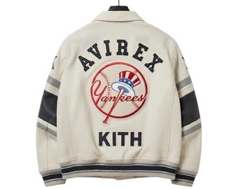 Peut inclure: Une veste universitaire blanc cassé avec des lettres bleu marine indiquant AVIREX et KITH. Le dos présente un grand logo brodé de baseball des New York Yankees avec un chapeau haut-de-forme patriotique. Les manches ont des rayures bleu marine et gris.