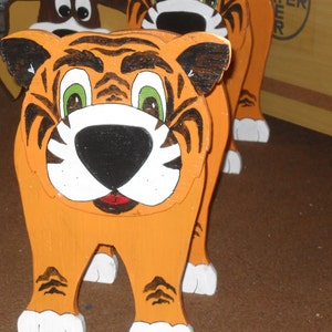 Peut inclure: Une figurine de tigre en bois avec des rayures orange et noires, des pattes blanches et un visage peint avec des yeux verts et un nez noir.