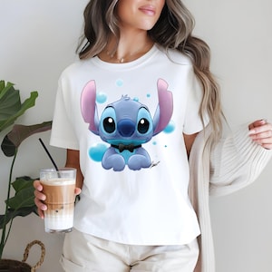 Pu&ograve; includere: Una t-shirt bianca a maniche corte con una stampa grafica di un personaggio alieno blu con grandi orecchie e un papillon nero. Il personaggio &egrave; circondato da bolle azzurre. La maglietta presenta un girocollo e una vestibilit&agrave; standard.