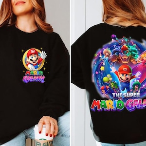 May include: Black sweatshirt featuring Mario from Super Mario Galaxy. The front has a circular graphic of Mario waving, with the words "Mario Galaxy." The back displays a larger, colorful graphic of Mario and other characters from the game.