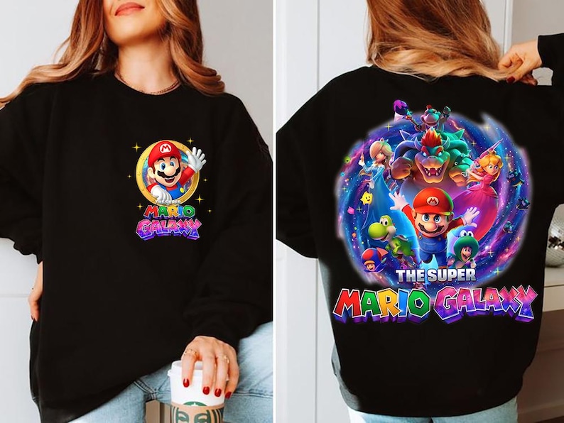 May include: Black sweatshirt featuring Mario from Super Mario Galaxy. The front has a circular graphic of Mario waving, with the words "Mario Galaxy." The back displays a larger, colorful graphic of Mario and other characters from the game.