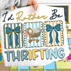 Puede incluir: Tela blanca con el texto "I'd Rather Be Thrifting". El diseño incluye un carrito de compras lleno de artículos vintage y dos lazos azules brillantes. El fondo tiene rayas azules y beige.