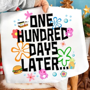 May include: White square pillow with the text "ONE HUNDRED DAYS LATER..." in black, with colorful cartoon graphics of a Krabby Patty, jellyfish, flowers, and a pineapple house. The pillow is held by a person.