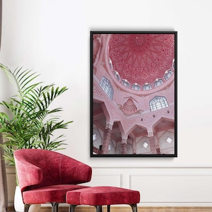 Może przedstawiać: Oprawiony wydruk wnętrza meczetu z dużą, ozdobną kopułą. Architektura charakteryzuje się skomplikowanymi wzorami i jest pomalowana w odcieniach różu. Obraz jest umieszczony na tle białej ściany, z czerwonym krzesłem i otomaną na pierwszym planie.