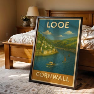May include: A framed travel poster for Looe, Cornwall, featuring a scenic illustration of a harbor town with a bridge, boats, and lush green hills. The poster has a blue sky and the words "LOOE" and "CORNWALL" in bold letters.