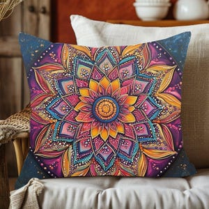 May include: Square decorative pillow with a vibrant mandala design. The pillow features a central yellow flower surrounded by intricate patterns in shades of pink, purple, blue, and orange. The corners have a dark blue background with gold speckles.