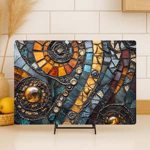 Puede incluir: Una pieza de arte de mosaico rectangular con un diseño vibrante. La obra presenta una mezcla de azulejos naranjas, azules y marrones, con acentos metálicos y patrones en espiral. Se exhibe sobre un soporte de metal negro.