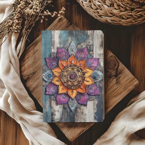 May include: A rectangular notebook featuring a printed cover with a central mandala design in shades of purple, orange, and teal. The background of the cover displays a weathered, vertical wood plank pattern in muted blue and gray tones.