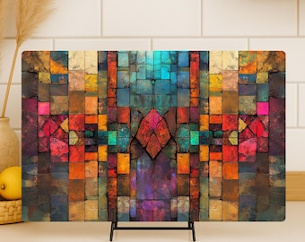 May include: A rectangular decorative cutting board with a colorful mosaic design. The mosaic features a symmetrical pattern of squares in shades of red, orange, blue, and purple. The cutting board is displayed on a black metal stand.