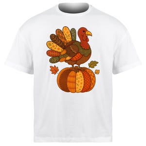 May include: White t-shirt with a Thanksgiving design. The graphic shows a turkey on a pumpkin, with autumn leaves. The turkey has a red head, brown body, and a colourful fan of feathers. The pumpkin is orange and brown, with a patchwork design.