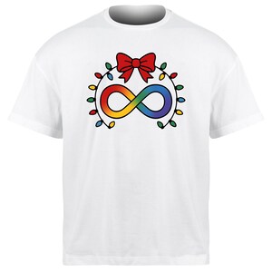 May include: White t-shirt featuring a rainbow infinity symbol, a red bow, and a string of colorful lights. The design is centered on the front of the shirt. The shirt has a crew neck and short sleeves.