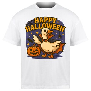 Op de afbeelding: Wit T-shirt met een Halloween-thema. Het heeft een cartoon gans in een vampierkostuum, een pompoen en de tekst "Happy Halloween". Het ontwerp bevat een vleermuis, een spin en sterren, allemaal tegen een donkerblauwe achtergrond.