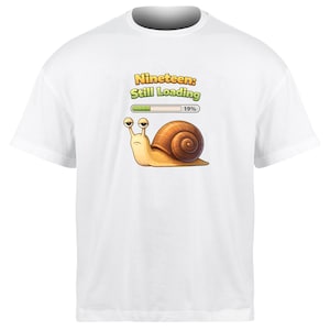 May include: White t-shirt featuring a cartoon snail with the text "Nineteen: Still Loading" above a loading bar at 19%. The snail is tan with a brown shell and large, expressive eyes.
