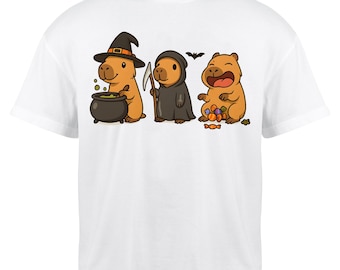 May include: White t-shirt featuring a Halloween-themed graphic. The design shows three cartoon capybaras dressed as a witch, the grim reaper, and a candy-loving character. The witch capybara stirs a cauldron, while the reaper holds a scythe.