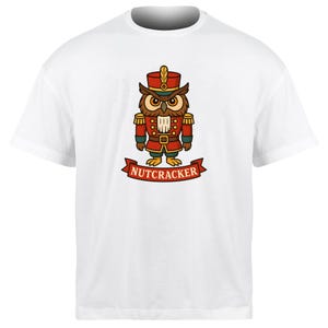 May include: White t-shirt featuring a cartoon owl dressed as a nutcracker. The owl wears a red hat, jacket, and pants with gold accents. A banner below reads "NUTCRACKER" in red letters.