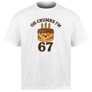 May include: White t-shirt with a graphic featuring a cartoon birthday cake with three lit candles and the text "Oh Crumbs I'm 67". The cake has a smiling face and chocolate frosting.