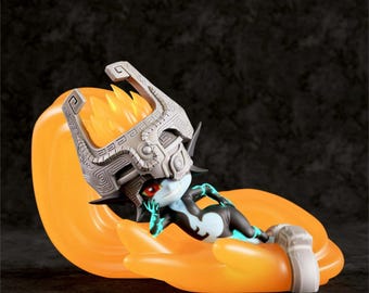 May include: A figurine of a character from The Legend of Zelda. The figure is lying on a large orange shape, wearing a detailed silver helmet and a black and blue bodysuit. The figure has red eyes and is posed with one hand on its chin.
