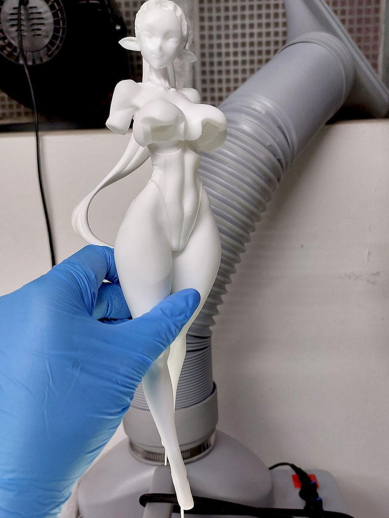 May include: A white 3D printed figurine of a female figure with long hair and pointed ears. The figure is wearing a one-piece outfit with a high neckline and a low-cut back. The figure is posed with one hand on her hip and the other arm extended.