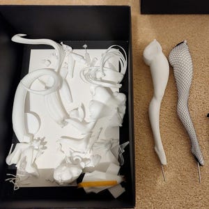 May include: A white plastic model kit of a female figure with various body parts and accessories. The kit includes a pair of legs with fishnet stockings, a pair of legs with a smooth finish, and a variety of other pieces.