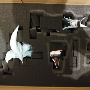May include: A figure is packaged in a box with foam padding. The figure is made of plastic and has a blue and white tail. The figure is wearing a black and white outfit.