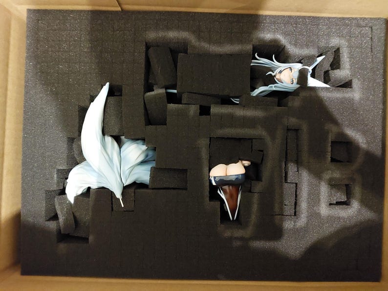 May include: A figure is packaged in a box with foam padding. The figure is made of plastic and has a blue and white tail. The figure is wearing a black and white outfit.