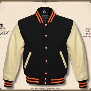 Peut inclure: Veste de style universitaire en laine noire avec des manches en cuir crème. Détails orange sur le col, les poignets et la taille. Poches avant et fermeture à boutons. Le texte "KHAN & CO. Jacket Handmade & Premium" est visible.