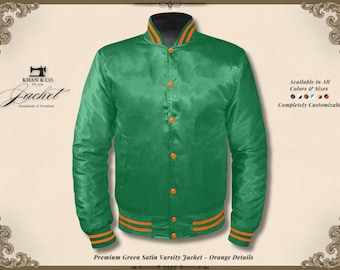 Puede incluir: Chaqueta universitaria de satén verde con detalles en naranja. La chaqueta tiene cierre de botones, puños acanalados y cuello con rayas naranjas. El texto "KHAN & CO. Jacket Handmade @ Premium" es visible. Completamente personalizable.