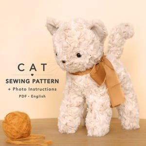 Op de afbeelding: Een beige pluche kattenspeeltje met een textuur van rozenkrullen, zwarte ogen en een bruin lint om de nek. Ernaast ligt een bol oranje garen. De tekst luidt: CAT SEWING PATTERN + Photo Instructions PDF • English.
