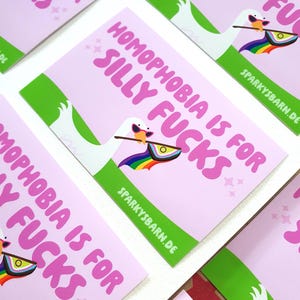 Könnte beinhalten: Rosa Karten mit dem Text "HOMOPHOBIA IS FOR SILLY FUCKS" in Rosa. Jede Karte zeigt eine Cartoon-Gans mit Sonnenbrille, die eine Regenbogenfahne hält. Die Karten haben einen grünen Rand und die Website "SPARKYSBARN.DE".