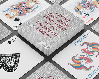 May include: A deck of playing cards with a newspaper-themed design. The card backs and the deck's top feature a newspaper print. The deck's top has the text "I DON'T LIKE BEING TOLD WHAT TO DO UNLESS I'M NAKED". Individual cards are visible.