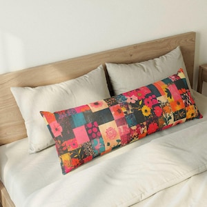 May include: A long, rectangular body pillow with a patchwork floral design. The pillow features squares of various colors, including pink, blue, and yellow, with floral patterns. The pillow is placed on a bed with white linens.