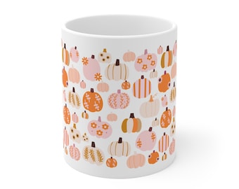 Könnte beinhalten: Ein weißer Keramikbecher mit einem sich wiederholenden Muster aus verschiedenen Kürbissen in Orange-, Hellrosa- und Cremetönen. Die Kürbisse sind mit diversen Motiven wie Streifen, Blumenakzenten und blättrigen Rankenillustrationen verziert.